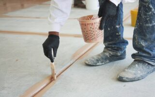 This image shows a man painting a floor with a paint brush.